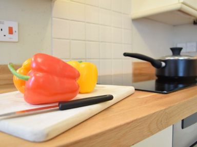 A kitchen countertop with a cutting board holding bell peppers and a knife next to a stove with a saucepan at Spindrift Southwold in Southwold