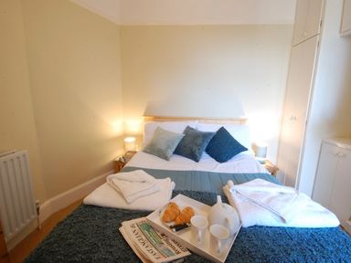 A bedroom with a made bed with blue cushions white towels a tray with teapot croissants and cups at Spindrift Southwold
