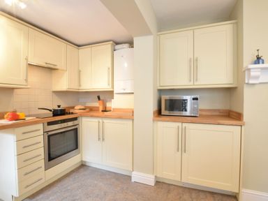 A kitchen with cream cabinets wooden countertops an oven a microwave and kitchen utensils at Spindrift Southwold