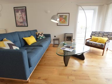 A living room with blue sofa and patterned armchair facing a glass coffee table at Aldeburgh Lodge Gardens in Aldeburgh