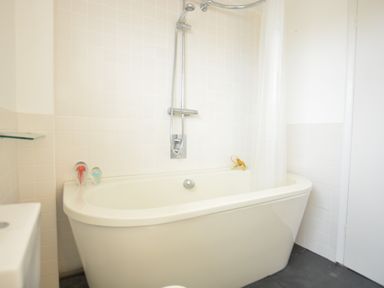 A bathroom with a bathtub shower and white tiled walls with two glass decorations at Aldeburgh Lodge Gardens in Aldeburgh