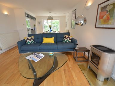 A living room with a blue sofa yellow and patterned cushions glass coffee table and a stove at Aldeburgh Lodge Gardens in Aldeburgh