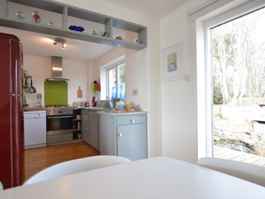 A kitchen with gray cabinets red refrigerator dishwasher and a window showing garden at Aldeburgh Lodge Gardens in Aldeburgh