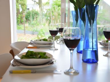 A dining table set with bowls of salad, glasses of red wine, and blue vases with green plants at Aldeburgh Lodge Gardens in Aldeburgh