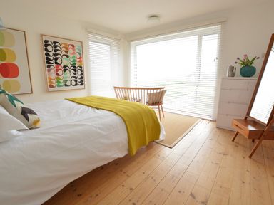 A bedroom with a bed a wooden chair a dresser with a vase of flowers and a standing mirror at Aldeburgh Lodge Gardens in Aldeburgh