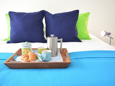 A bed with blue and green pillows and a wooden tray holding a teapot croissants and cups at Aldeburgh Lodge Gardens in Aldeburgh