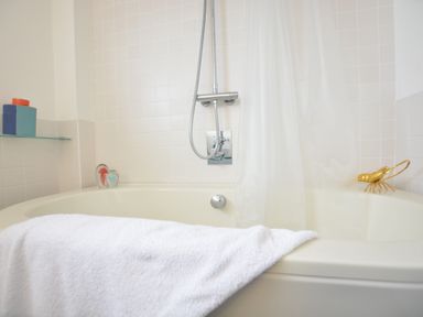 A bathtub with a white towel draped over the edge and a showerhead mounted on tiled wall at Aldeburgh Lodge Gardens in Aldeburgh