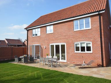 A backyard patio with tables chairs and a lounge chair outside a brick house with tiled roof at Meadowsweet Blythburgh near Reydon