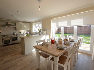 A kitchen and dining area with a wooden table set for breakfast and a view of the garden through glass doors at Meadowsweet Blythburgh in Blythburgh near Reydon