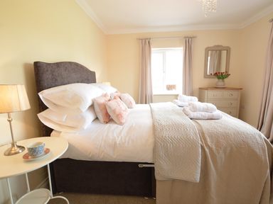 A bedroom with a made bed pillows and towels bedside table with a lamp and cup chest of drawers with a mirror and flowers Meadowsweet Blythburgh Blythburgh near Reydon