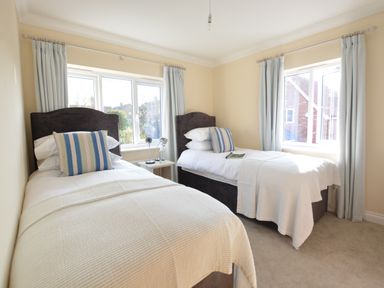 A bedroom with two single beds striped pillows curtains and a bedside table with lamps at Meadowsweet Blythburgh near Reydon