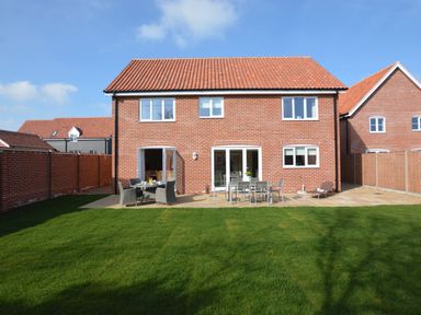 A brick house with a tiled roof and a patio with outdoor furniture in a fenced backyard at Meadowsweet  Blythburgh near Reydon