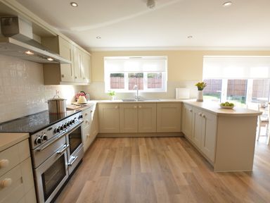 A kitchen with cabinets a stove a kettle a pot a sink and a countertop with a bowl of fruit and flowers at Meadowsweet Blythburgh near Reydon