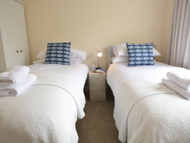 A bedroom with two single beds with white covers and blue fish pattern pillows at Meadowsweet Blythburgh near Reydon