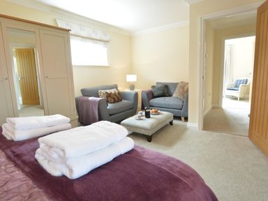 A bedroom with folded towels on a bed two armchairs a small table and an ottoman with coffee and pastries at Meadowsweet Blythburgh in Blythburgh near Reydon