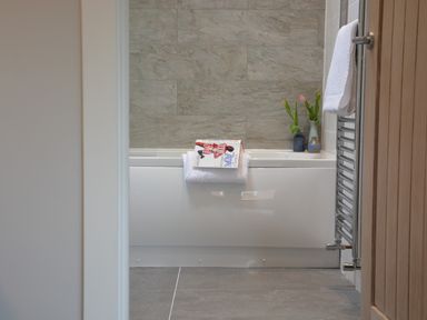 A bathroom with a white bathtub a towel hanging on the side and flowers in vases on the edge at Milk Parlour Spexhall Near Halesworth