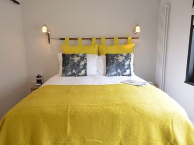 A bedroom with a yellow bedspread blue tie dye pillows and wall lamps at Milk Parlour in Spexhall Near Halesworth