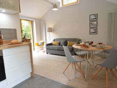 An open plan kitchen and dining area with a round table set for breakfast and a grey sofa at Milk Parlour Spexhall Near Halesworth