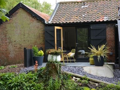 A brick building with black wooden shutters and a tiled roof with potted plants and outdoor chairs at Milk Parlour Spexhall Near Halesworth
