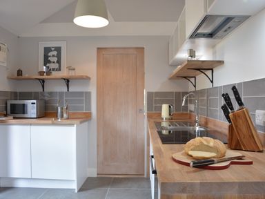 A kitchen with wooden countertops a loaf of sliced bread a knife a microwave kettle and a set of knives at Milk Parlour in Spexhall Near Halesworth