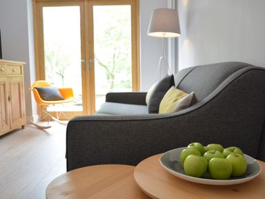 A living room with a gray sofa with cushions a wooden side table with green apples a standing lamp a yellow rocking chair wooden cabinet and glass doors at Milk Parlour in Spexhall Near Halesworth