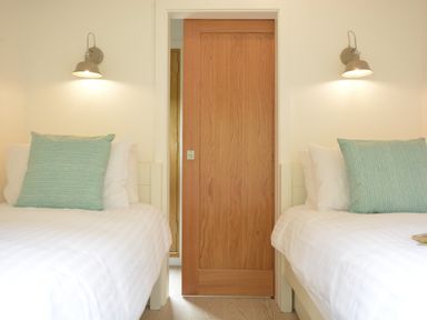 A bedroom with two single beds with white bedding and green pillows and a wooden sliding door in between at Red Poll Barn Spexhall Near Halesworth