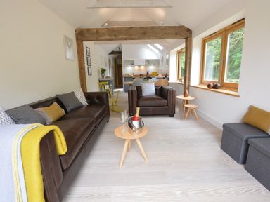 A living room with brown leather sofas and small round wooden tables at Red Poll Barn Spexhall Near Halesworth