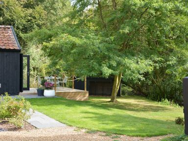 A garden with a tree, patio furniture, and a black wooden building at Red Poll Barn in Spexhall Near Halesworth