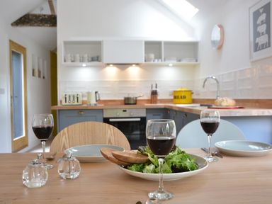 A kitchen with a wooden dining table set with plates glasses of red wine and a bowl of salad at Red Poll Barn in Spexhall Near Halesworth
