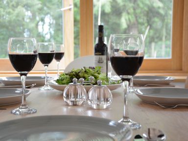 A dining table set with wine glasses filled with red wine plates cutlery a bowl of salad salt and pepper shakers and a bottle of wine at Red Poll Barn Spexhall Near Halesworth