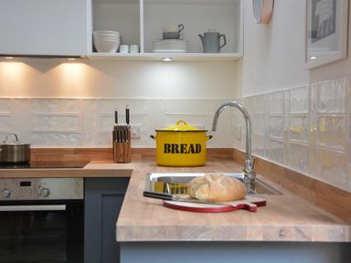 A kitchen counter with a sink, yellow bread container, knife block, stovetop, and bread on a cutting board at Red Poll Barn Spexhall Near Halesworth