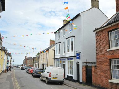 A street with parked cars and buildings with colorful flags hanging above at Walton House Southwold