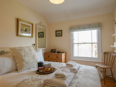 A bedroom with a bed laden with towels and breakfast tray beside a wooden chest of drawers and window at Walton House Southwold