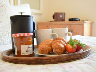 A breakfast tray with croissants strawberries jam a black coffee pot and two mugs on a bed at Walton House Southwold