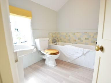 A bathroom with a toilet with wooden seat a bathtub with a white towel and a sink near a window with a yellow blind at Walton House Southwold
