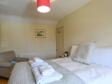 A bedroom with a bed with white sheets and towels and a beige armchair in the corner at Walton House Southwold