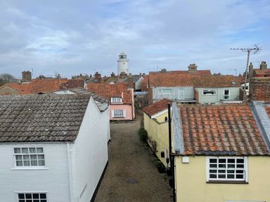 A narrow street lined with houses with tiled roofs and a lighthouse in the background at Walton House Southwold