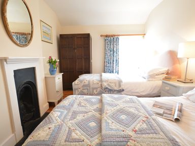 A bedroom with two single beds with patchwork quilts a wooden wardrobe a bedside table with a lamp and books a small fireplace and a floral curtain at Walton House Southwold