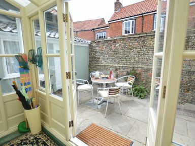 A patio with a table and chairs by a stone wall viewed through open glass doors at Walton House Southwold