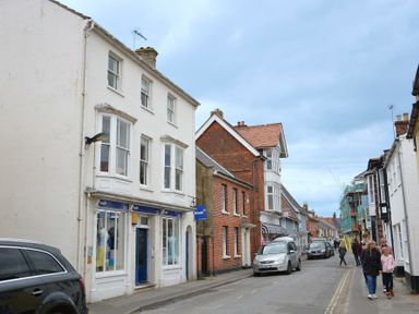 A street with parked cars and pedestrians walking by shops and houses in Southwold