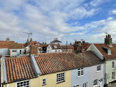 Rooftops of houses with tiled roofs and chimneys under a partly cloudy sky in Southwold