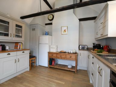 A kitchen with wooden floor cabinets a white refrigerator wooden table with kitchen items and exposed ceiling beams at Walton House Southwold