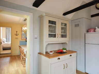 A kitchen cabinet with glass doors and a wooden countertop with bowls of vegetables and a red pepper next to a fridge and a doorway leading to a dining room and bedroom at Walton House Southwold