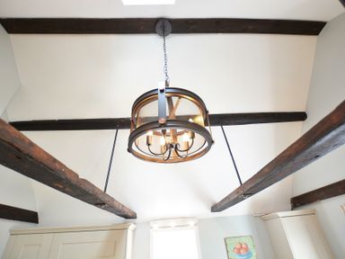 A ceiling with dark wooden beams and a round metal chandelier hanging in the middle at Walton House Southwold
