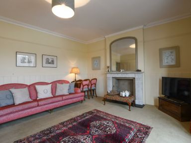 A living room with a red sofa and cushions a fireplace with a mirror above a patterned rug and a television on a wooden stand at Walton House Southwold