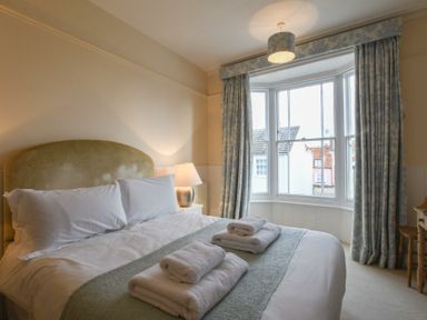 A bedroom with a bed and folded towels on it by a bay window with curtains at Walton House Southwold