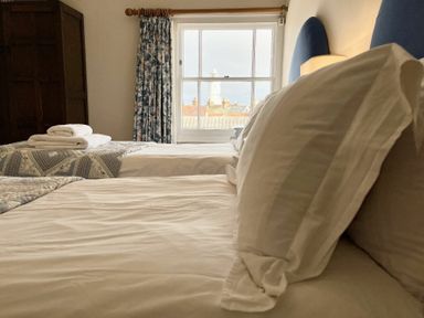 A bedroom with two beds a window with floral curtains and a view of rooftops and a lighthouse at Walton House Southwold