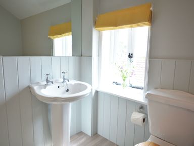 A bathroom with a white pedestal sink a toilet a window with a yellow blind and flowers on the windowsill at Walton House Southwold