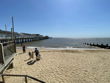 A sandy beach with three people walking near the water and a long pier extending into the sea at Walton House Southwold