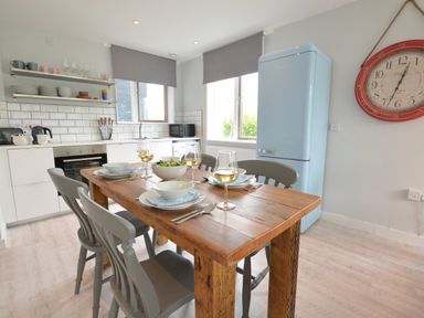 A kitchen with a wooden dining table set for four with bowls and glasses at Sweet Pea Southwold